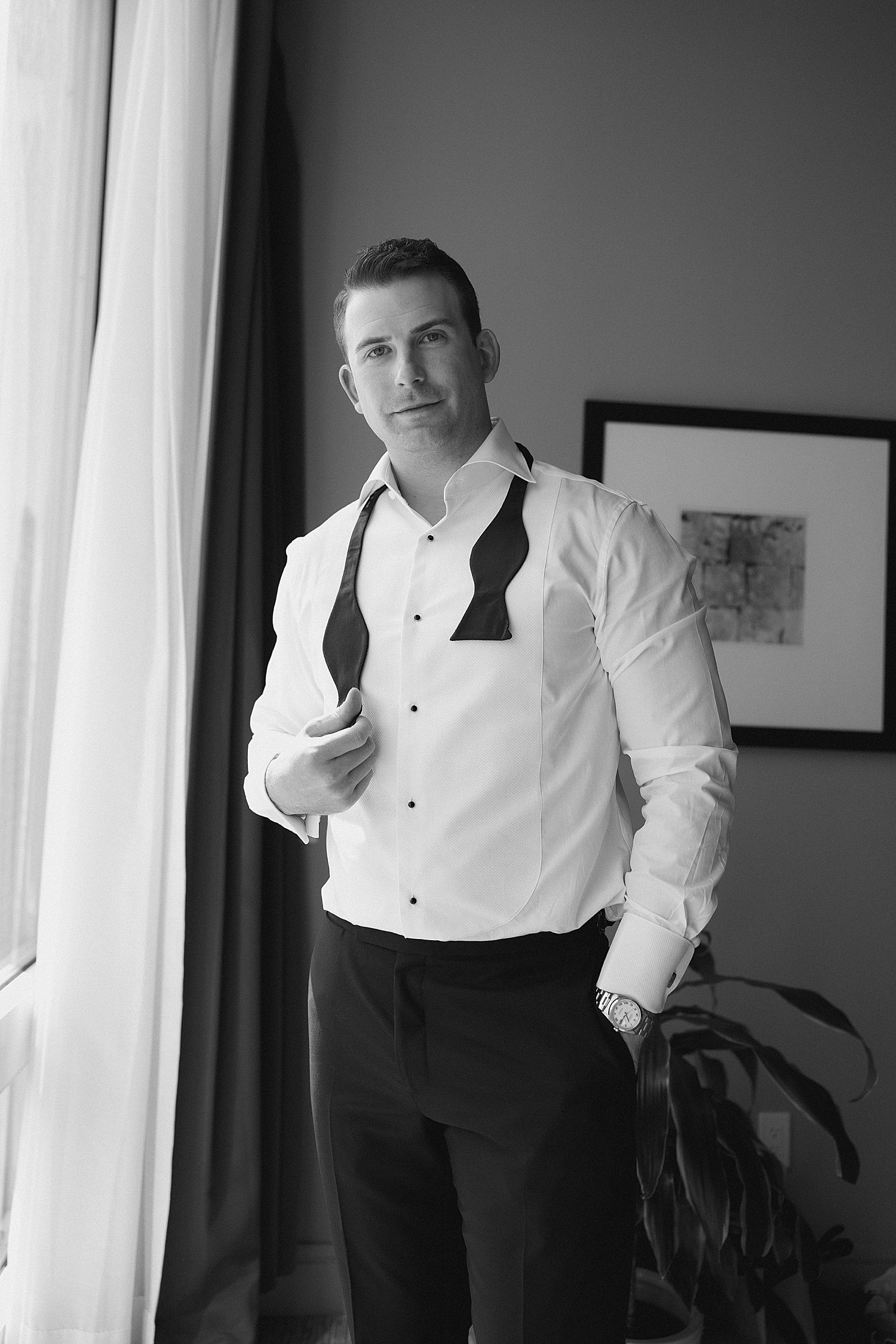 groom stands next to window getting ready for day at RPM Events