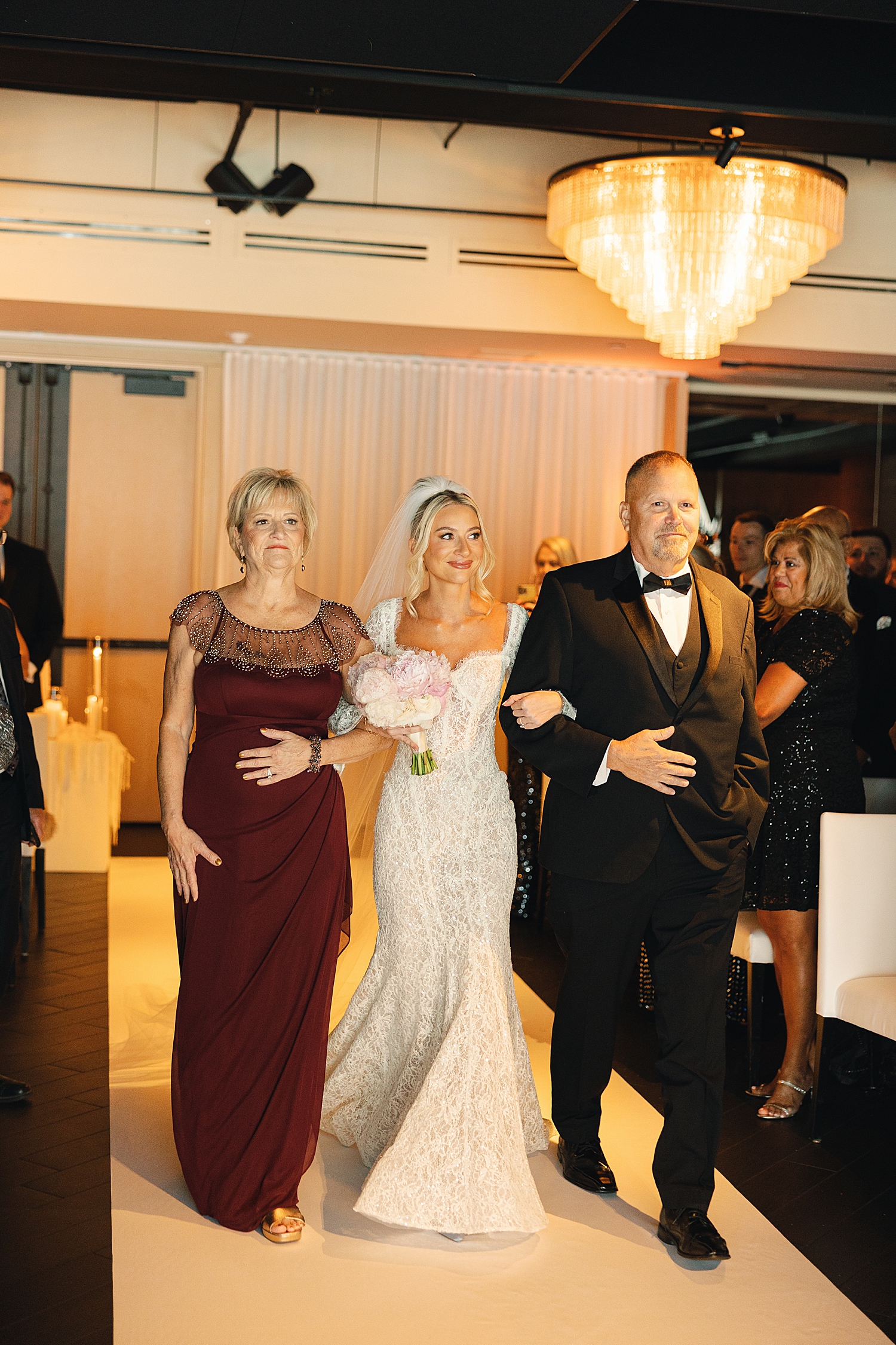 bride walks down the aisle with both parents by Rachel Andrade Photography