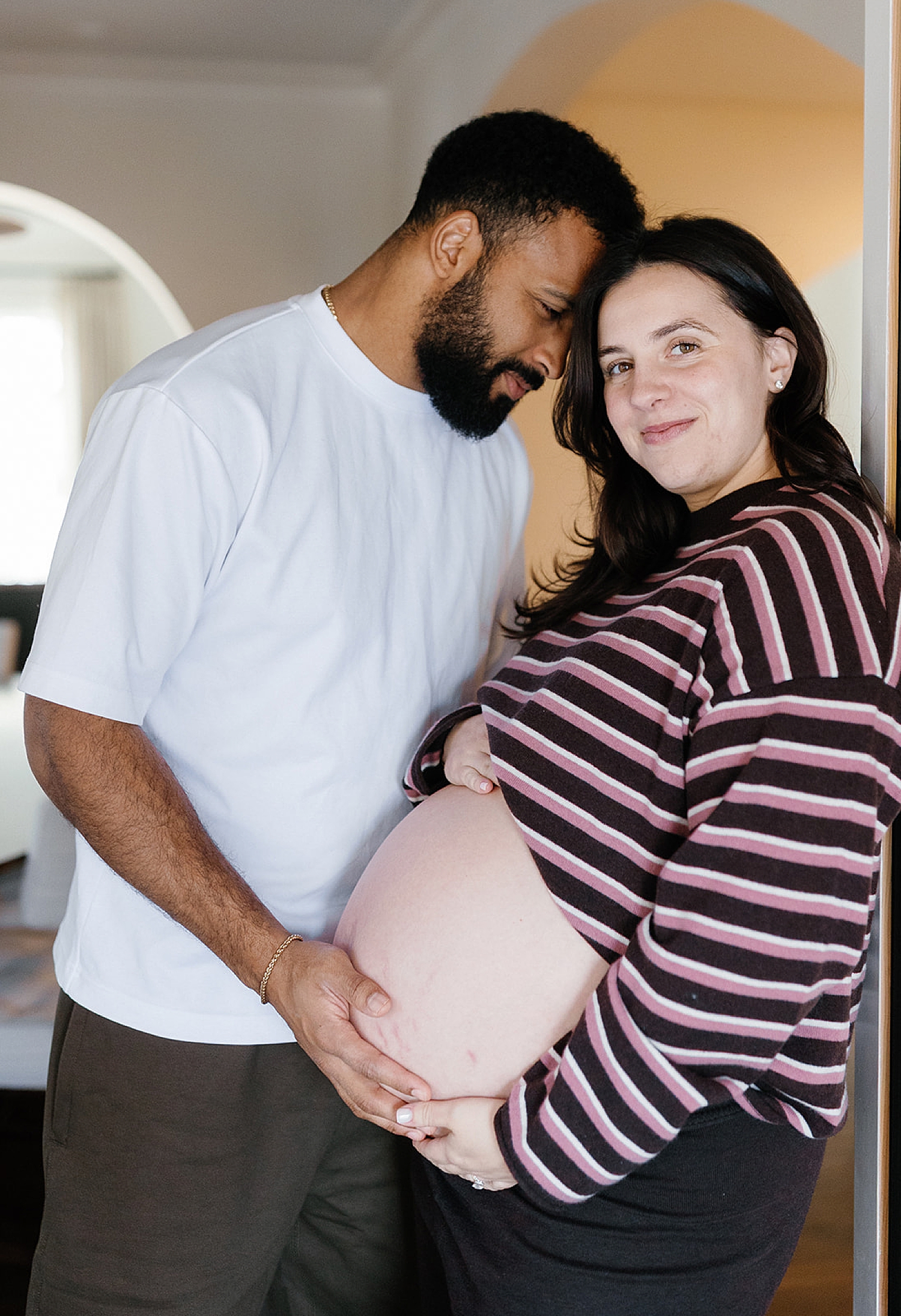 expecting mom leans against the wall, husband cradling her bump after learning how to style your family session