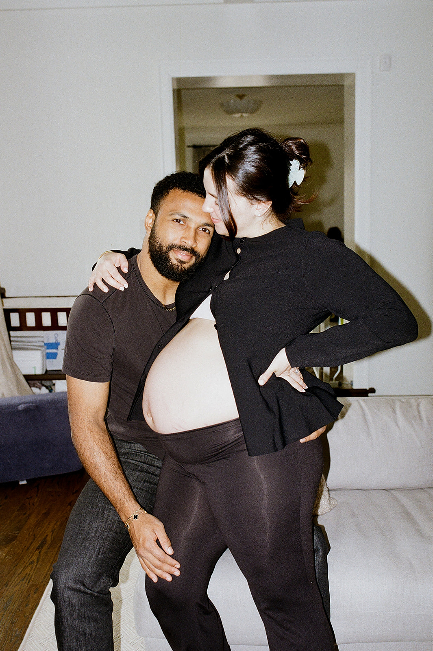 mom and dad stand next to a couch wearing black clothing after figuring out how to style your family session
