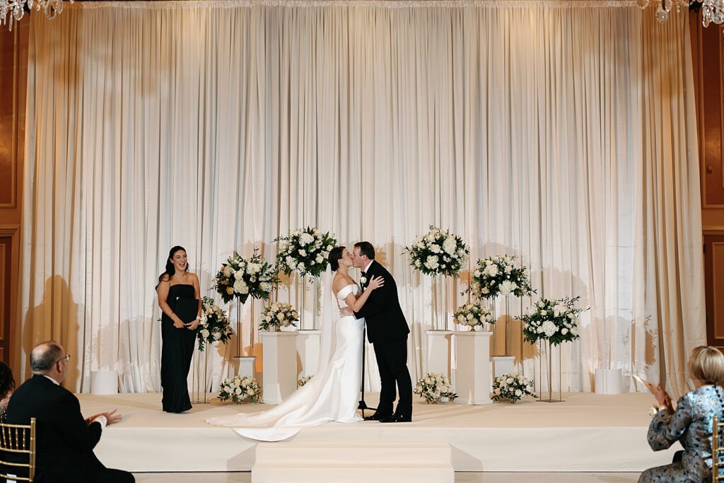 newlyweds share a kiss at the alter in front of drapery by Rachel Andrade Photography